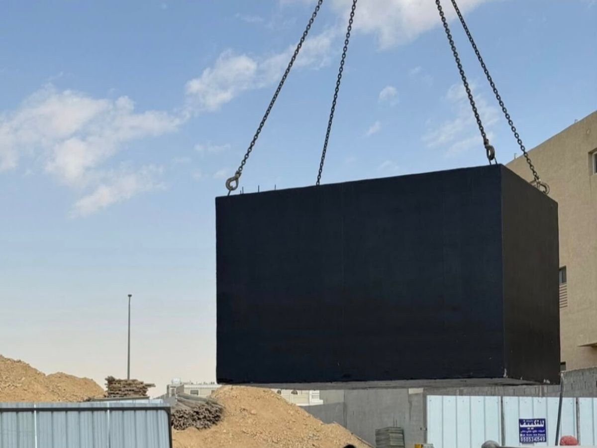 A precast reinforced concrete water tank being lowered by crane on site